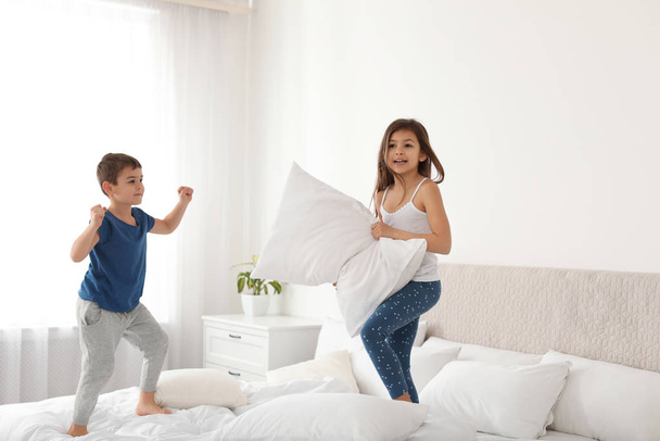 Happy children having pillow fight in bedroom - 写真・画像