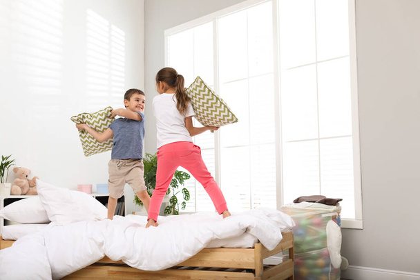 Happy children having pillow fight in bedroom - Фото, изображение