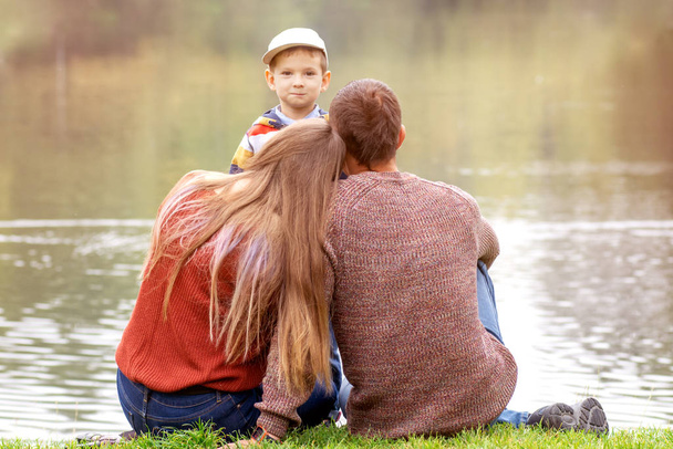 Щаслива сім'я тримає руки, сидячи на зеленому газоні на відкритому повітрі, маючи якісний час разом
. - Фото, зображення