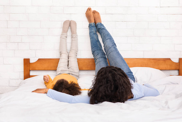 Mother And Daughter Lying On Bed With Raised Legs Indoor - Foto, afbeelding