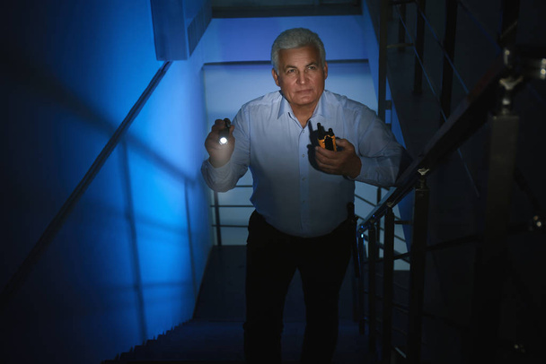Professional security guard with flashlight on stairs in dark ro - Foto, imagen