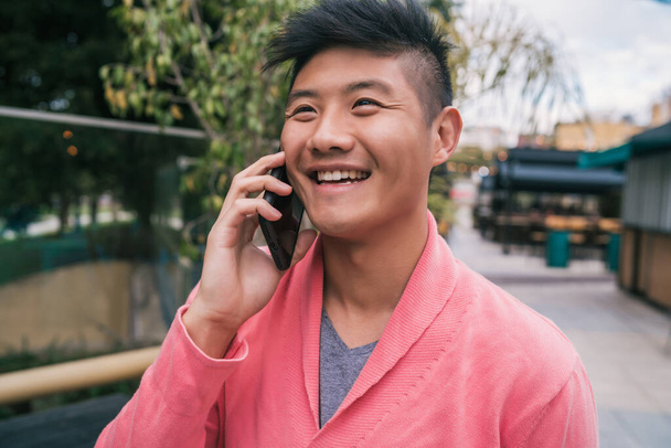 Asian man talking on the phone outdoors. - 写真・画像