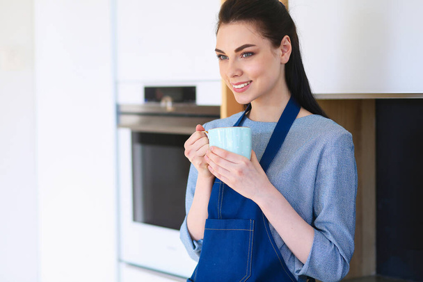 Portrait of young woman with cup against kitchen interior background - Foto, immagini