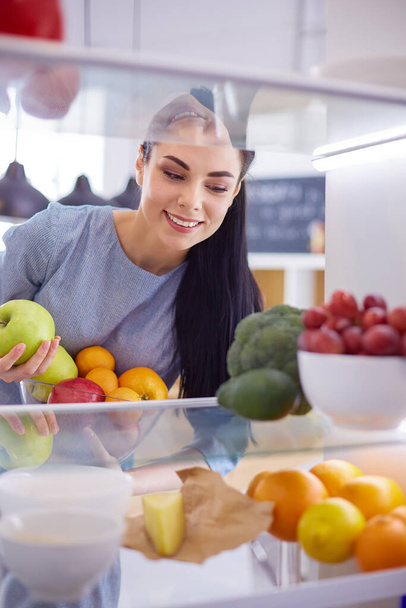 Smiling woman taking a fresh fruit out of the fridge, healthy food concept - Φωτογραφία, εικόνα