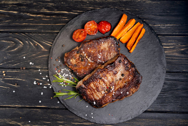 juicy piece of fried meat lies on a stone plate against a black wooden table - Foto, Bild