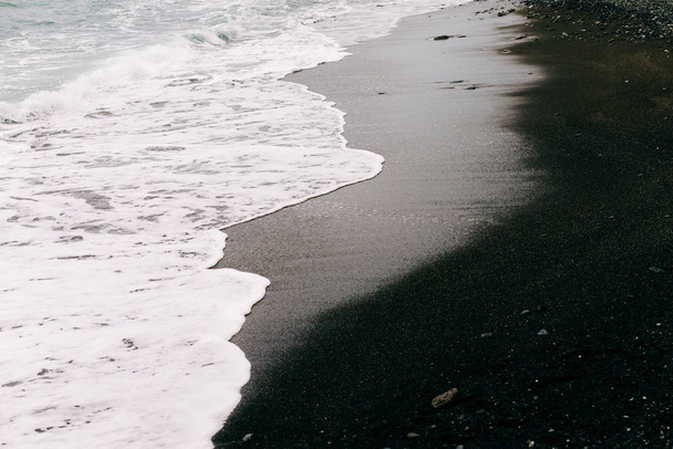 uma onda do mar chega na costa com areia vulcânica preta. belo fundo natural na Islândia
 - Foto, Imagem