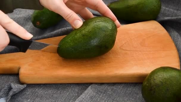 As mãos femininas cortam o abacate na metade. Abacate com pontos pretos. Abacate maduro fresco - Filmagem, Vídeo