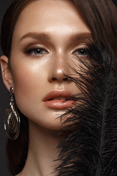 A beautiful girl with evening make-up, a Hollywood wave and a black feather in her hand. Beauty face. - Foto, immagini