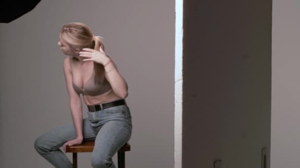 backstage de chica caucásica con el pelo largo posando en sujetador beige, jeans en estudio
 - Metraje, vídeo