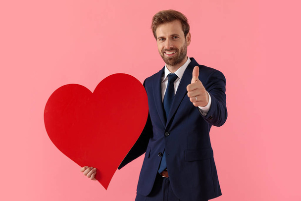 Businessman holding a heart shape and giving a thumbs up - Zdjęcie, obraz