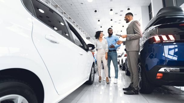 Afro Salesman Selling Car To Customers Standing In Dealership Showroom - Φωτογραφία, εικόνα