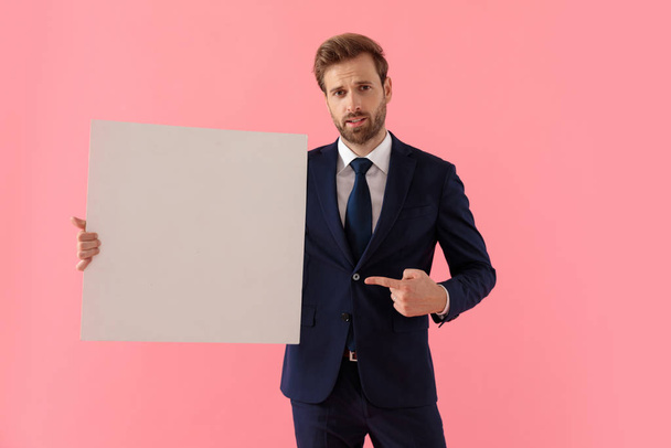 Unsure businessman holding a blank billboard and pointing to it  - Photo, Image