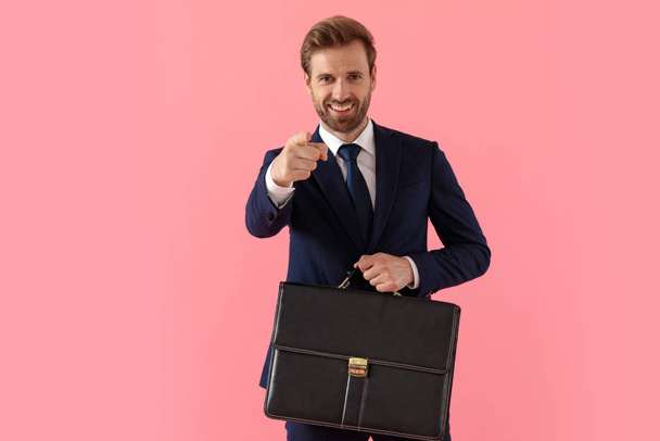 Hombre de negocios alegre señalando hacia adelante y sosteniendo un maletín
 - Foto, imagen