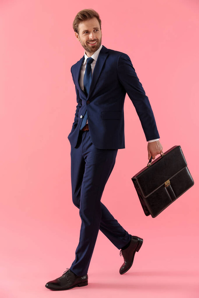 Γοητευτικός επιχειρηματίας κρατώντας ένα χαρτοφύλακα και το χέρι του στην τσέπη - Φωτογραφία, εικόνα