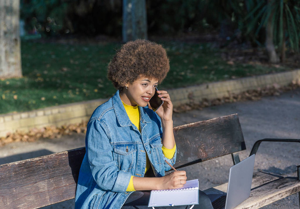 Mixte fille de race avec chemise en denim bleu parle par son smartphone assis dans un parc
 - Photo, image