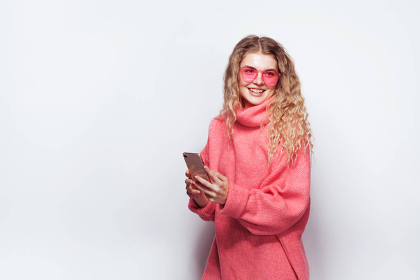 Beautiful joyful woman in pink sweater and sunglasses with smart - Foto, imagen