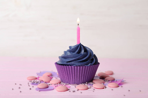 Delicious birthday cupcake with cream and burning candle on pink table - Фото, изображение