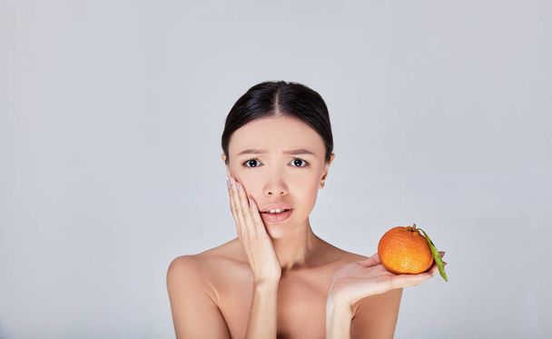 A surprised Asian woman holds an orange in her hand. - Fotoğraf, Görsel