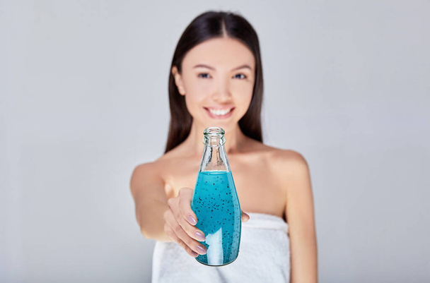 A cute Asian woman after a shower drinks a fruit cocktail of blue color. - Foto, imagen