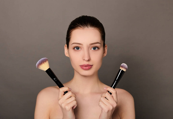 A young beautiful white girl with bare shoulders holds makeup brushes. - Foto, Imagem