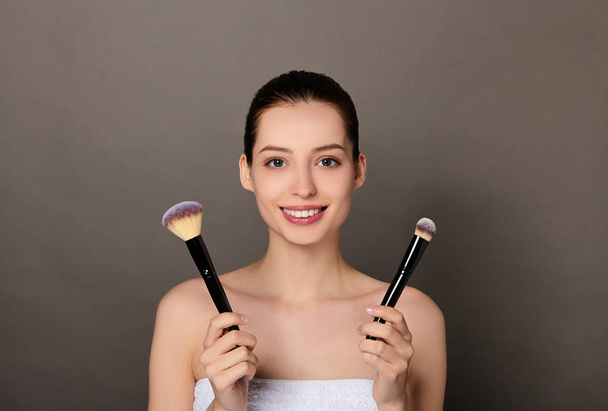Image of jwoman smiling at camera and using makeup brush. - Zdjęcie, obraz