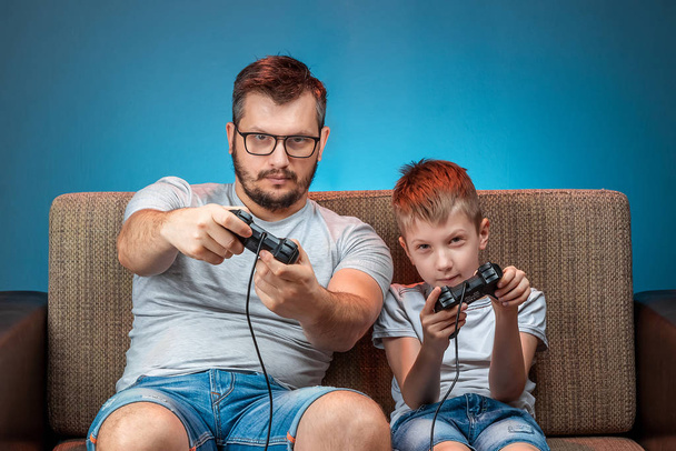 A cheerful family, dad and son play on the console, in video games, emotionally react while sitting on the couch. Day off, entertainment, leisure, spend time together. - Foto, Imagem