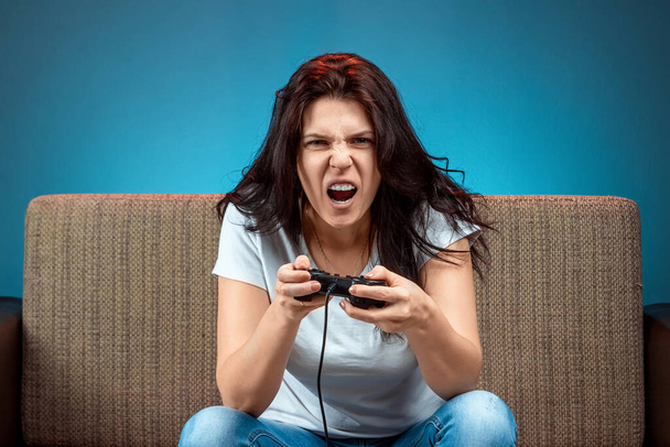 A cheerful girl plays on the console, in video games, emotionally react while sitting on the couch. Day off, entertainment, leisure. - Φωτογραφία, εικόνα