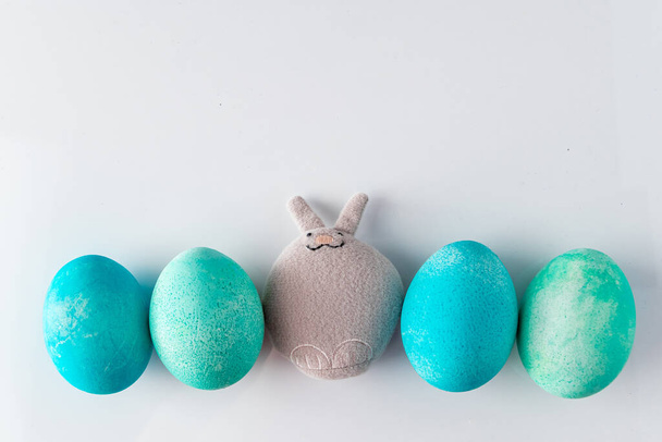 Huevos azules de Pascua y conejo de juguete sobre un fondo blanco. Lindo juguete conejito de Pascua y huevos pintados de azul con plumas sobre un fondo blanco. Lugar para su texto
. - Foto, Imagen