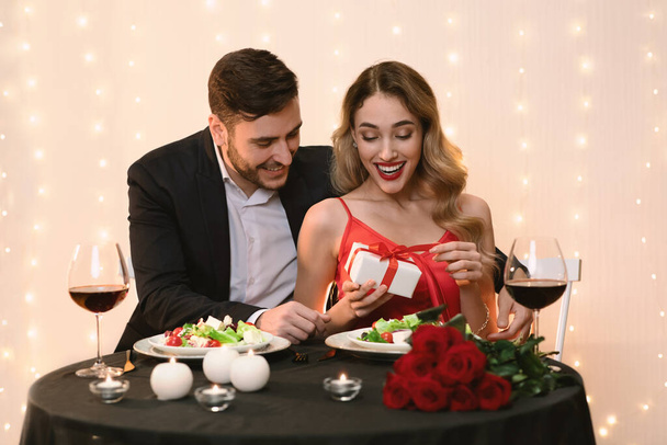 Happy girl receiving surprise present from boyfriend at dinner in restaurant - Photo, Image