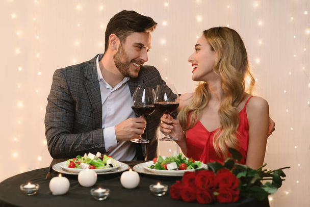 Restoranda kırmızı şarap kadehleriyle romantik genç bir çift. - Fotoğraf, Görsel