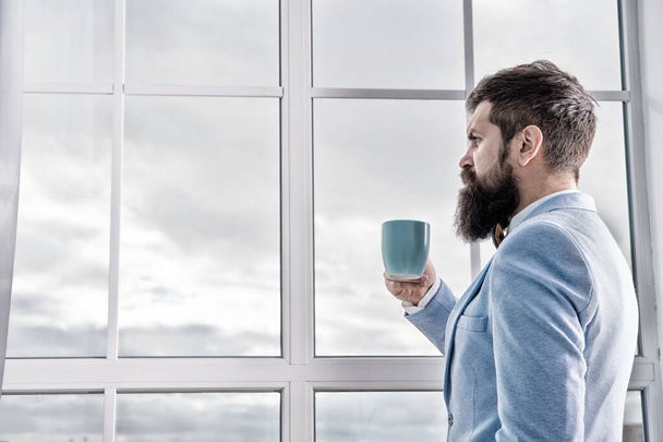 His big day. Wedding morning concept. Wedding day. Groom bearded hipster man wear blue tuxedo and bow tie. Man stand at window nervous about wedding. Life choices and expectations. But first coffee - Foto, Imagen