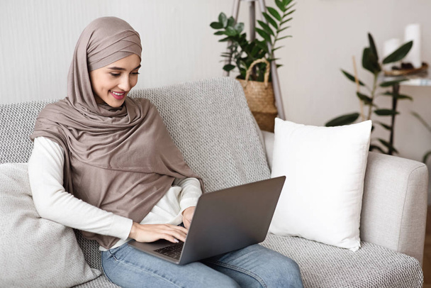 若いですイスラム教徒女性でヒジャーブ州でラップトップコンピュータを使用して自宅で - 写真・画像