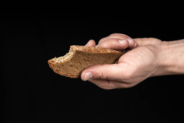 Man holds a bitten bread in his hand on black background - Valokuva, kuva