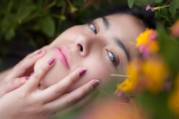 portrait of woman in the foreground with hands on her face among yellow flowers - Photo, Image