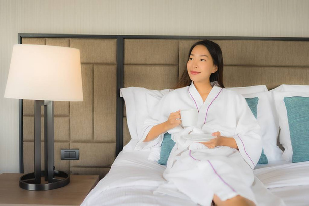 Portrét krásné mladé asijské ženy s šálkem kávy na posteli - Fotografie, Obrázek