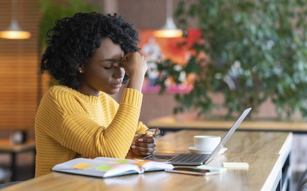 Уставшая черная девушка сидит перед ноутбуком в кафе
 - Фото, изображение