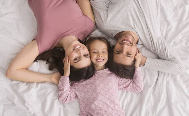 liebevolle Eltern und kleine Tochter liegen zusammen im Bett, Draufsicht - Foto, Bild