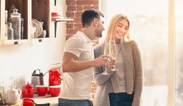Nuori pari juo samppanjaa ja hymyilee keittiössä
 - Valokuva, kuva