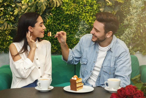 Человек кормит свою подругу дегустационным тортом, сидя в кафе
 - Фото, изображение