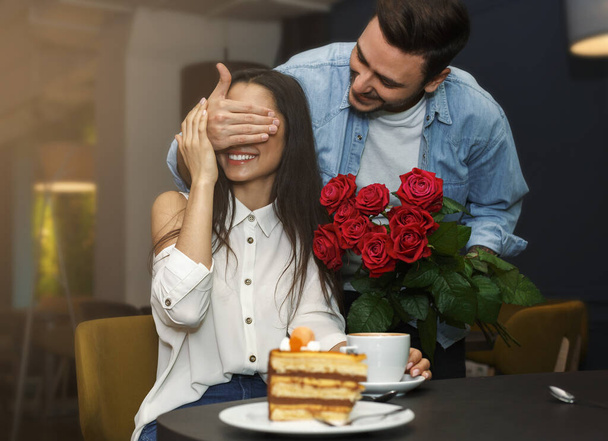Kochający mężczyzna zakrywający dziewczyny oczy dając jej bukiet w kawiarni - Zdjęcie, obraz