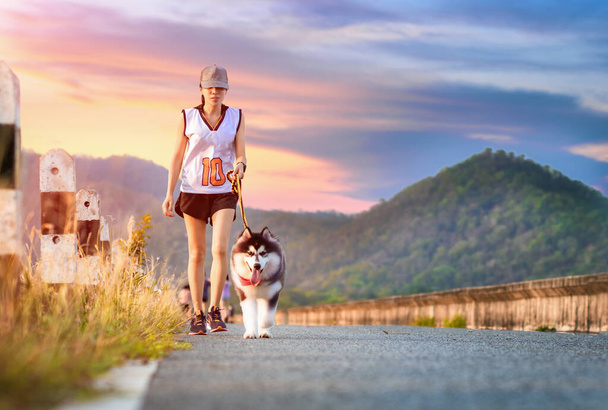 Woman doing daily exercise jogging on the public park road with puppy breed dog - Fotoğraf, Görsel