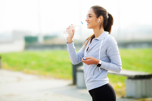 Kaunis nainen juo vettä ja kuunnella musiikkia juoksun jälkeen
 - Valokuva, kuva