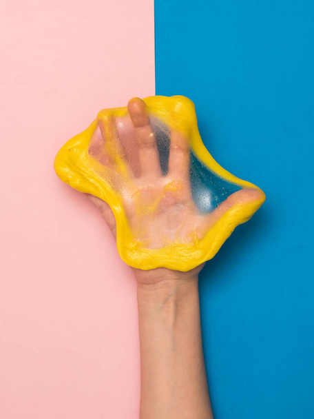 A torn yellow slime on the palm of your hand on a pink and blue background. - Photo, Image