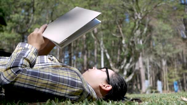 junge Asiatin entspannt sich und liest am Urlaubstag ein Buch, das auf Gras im Garten liegt. - Filmmaterial, Video