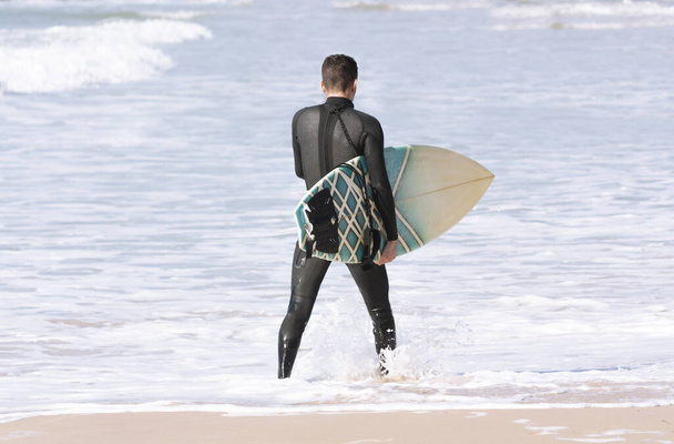 Sörf tahtası olan bir sörfçü suyun kenarında yürüyor. - Fotoğraf, Görsel