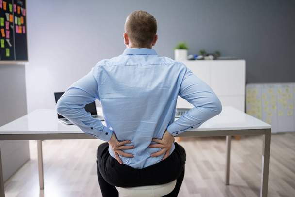 Young Businessman Having Back Pain While Sitting At Office Desk - Фото, изображение