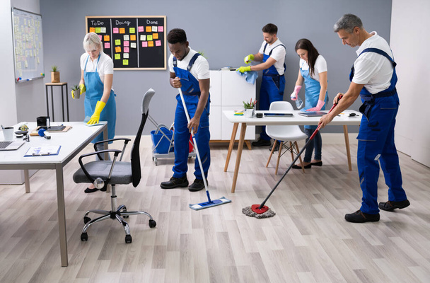 Group Of Janitors In Uniform Cleaning The Office With Cleaning Equipment - Фото, изображение