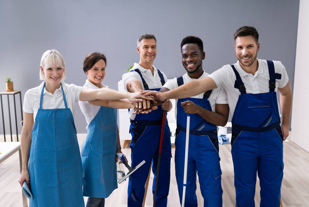 Portrait Of Happy Diverse Janitors In The Office With Cleaning Equipment Stacking Hands - Фото, зображення