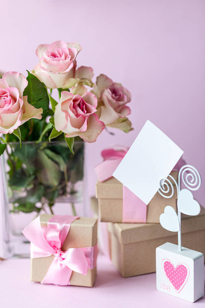 Business card, holiday card with a bouquet of flowers on a pink background. Gift box with a pink bow. Gift for Valentine's Day or March 8th. Vertical photo. Copy space. - Foto, afbeelding