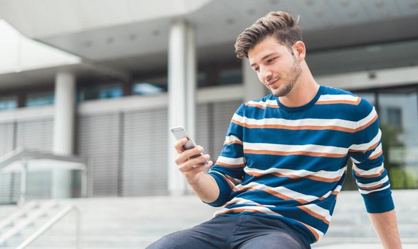 Young man sitting relaxed checking his smartphone messages - Foto, Bild